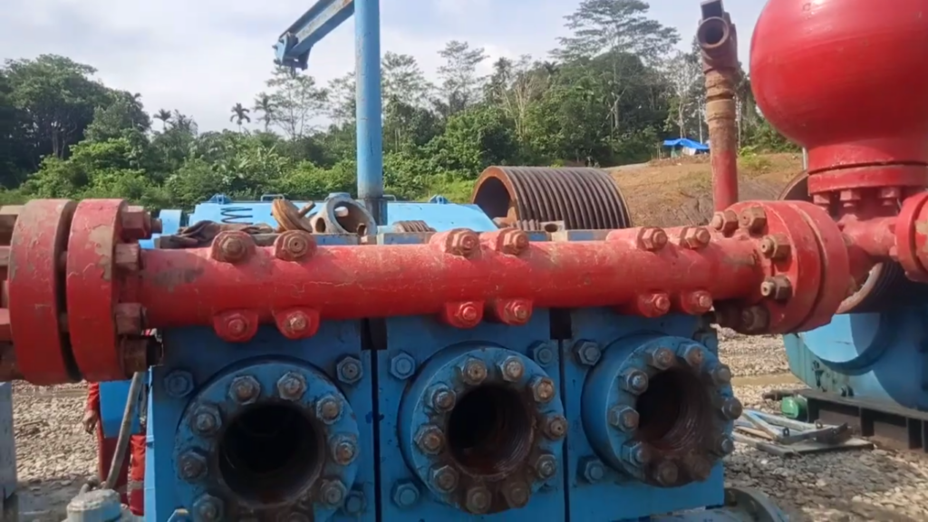 A red and blue duplex mud pump at a drilling site, with visible discharge pipes and fluid chambers.